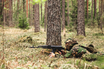Soldier male lying shooting from weapon near tree in forest nature, dressed in military camouflage...