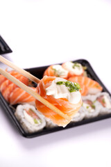 holding a piece of sushi close-up with chopsticks with oriental food tray blurred on white background