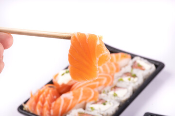 holding a piece of sashimi with chopsticks and blurred sushi tray in the background close-up