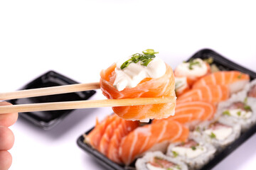 holding a piece of sushi with chopsticks with blurred oriental food tray on white background