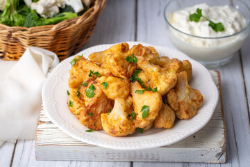 Fried in batter Cauliflower florets served on a black plate on a grey concrete table with ingredients, view from above, close-up, flatlay, copy space (Turkish name; karnabahar kizartmasi)