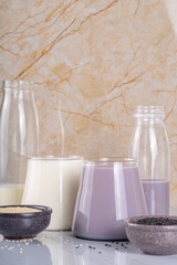 Black and white sesame milk, Alternative vegan non-dairy milk drink on glass and bottles with sesame seeds on light stone background. Raw food, vegetarian natural organic food diet