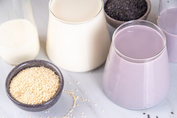 Black and white sesame milk, Alternative vegan non-dairy milk drink on glass and bottles with sesame seeds on light stone background. Raw food, vegetarian natural organic food diet