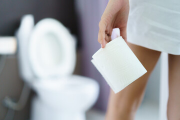 Asian young woman having a stomachache and food poisoning and getting to the toilet or restroom. Woman pick up a roll of tissue paper to the toilet. - obrazy, fototapety, plakaty