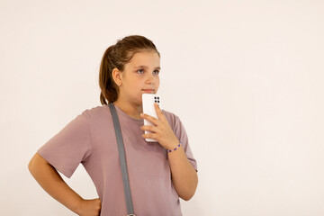 A beautiful teenage girl uses a smartphone against a white wall background. Summer concept.The style of the Zoomer generation. Concept of social networks