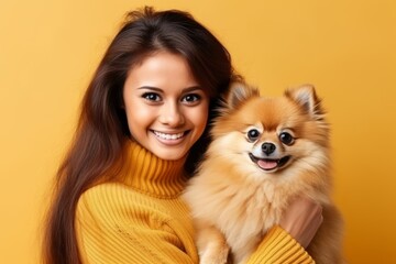 Horizontal shot of happy Afro American hostess poses with cute spitz puppy with stucked out tongue, looks aside and smiles, have nice walk together, isolated on yellow background, blank space