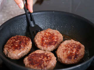A person flipping over beef patties with a spatula. Close up.