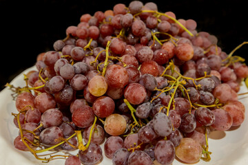 Red grapes on a white plate on a black background