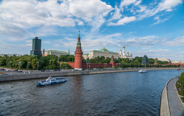 Fototapeta premium View of Kremlin with Vodovzvodnaya tower, Grand Kremlin Palace from repaired Bolshoy Kamenny Bridge in Moscow city on sunny summer day. Cruise ship sails on the Moscow river