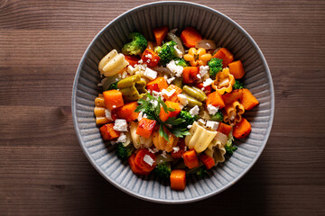 Autumn pasta salad with roasted pumpkin, broccoli, feta cheese on dark wooden background, fall season salad