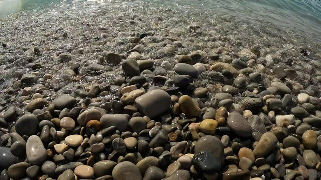 Waves rolling up onto rocks at the beach in Nice, France viewing the polished stones.
