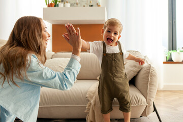 young mother high-fives her little son at home, woman rejoices and plays with her child by clapping...