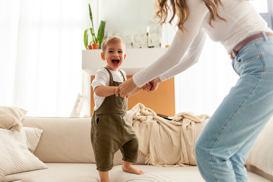 young mother dances and jumps with her son on the sofa, woman plays with her child at home, 2 year old boy rejoices