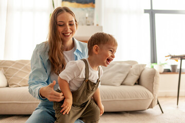 young mother dancing with her little son at home and laughing, woman playing with her child in the room