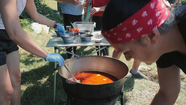 Distribution of food to hungry homeless, refugees. Volunteers scoop red soup, borscht, bograch with a ladle, donate and distribute food to the homeless and needy. Close up