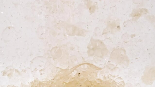 Macro Shot of Particles made of Powder, Cosmetic Texture in Water Descend up on White Background. Slow Motion. Brown Chocolate Protein Powder. Production of Natural Cosmetics. High quality FullHD 