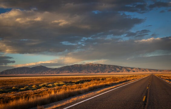 long straight desert road during sunset, Image shows the road in the Nevada desert during the golden hour giving off a beautiful scenic view of the desert and the mountains