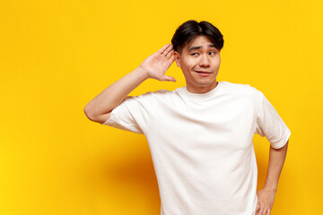 curious young guy asian student eavesdropping on a secret on yellow isolated background