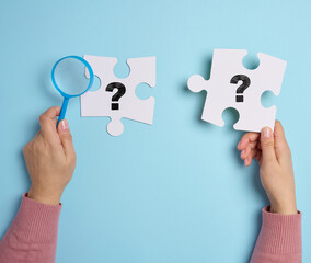 White puzzles with a question mark and a female hand holding a plastic magnifying glass, symbolizing the search for answers and solutions
