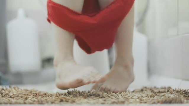 A woman is sitting on the toilet in a home bathroom, experiencing pain and suffer. Close-up of legs with red underpants. The concept of constipation, cystitis and diarrhea