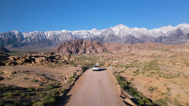 Cinematic aerial shot of white SUV driving down dirt road in Alabama Hills in California, USA