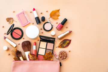 Cosmetic bag with make-up beauty products and autumn leaves at pastel background. Flat lay with space for text.