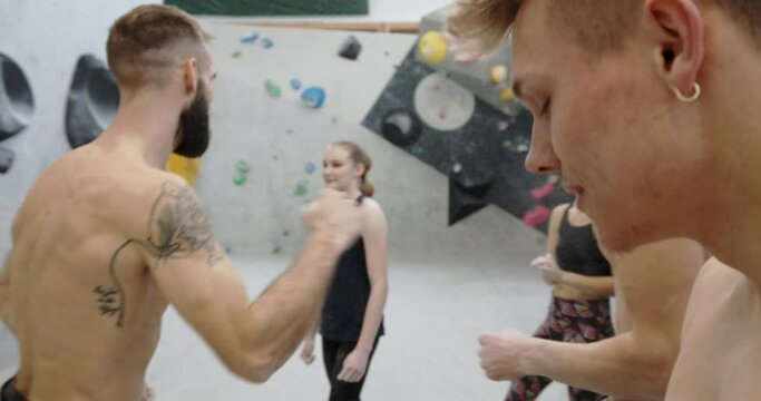 Fit group of young people in sportswear smiling and fist bumping together after a rock climbing session in a gym