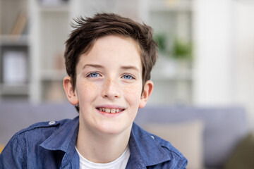 Portrait of happy brunette teenage guy in braces sitting in bright room, smiling and looking at camera.