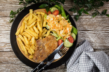 Fried pork chop in breadcrumbs, served with fries and salad.