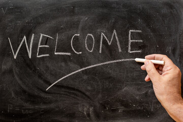 Mano escribiendo la palabra welcome con una tiza en la pizarra