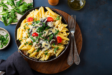 Penne pasta with mushroom sauce in a frying pan on the table, vegetarian comfort food top view copy space for text
