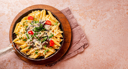 Penne pasta with mushroom sauce in a frying pan on the table, vegetarian comfort food top view copy space for text