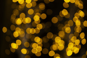 Christmas golden glowing background. Golden festive abstract shiny defocused background with flashing garlands. Tinsel blurred gold bokeh on a black background.