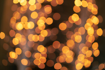 Christmas golden glowing background. Golden festive abstract shiny defocused background with flashing garlands. Tinsel blurred gold bokeh on a black background.