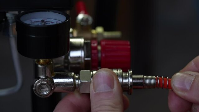 Worker connects orange air hose to air compressor via hose coupling, closeup. Spiral hose for supplying air pressure to the instrument and possibility of working at large distance from the main base