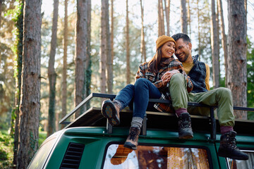 Cheerful couple relaxing on rooftop of their travel van in nature.