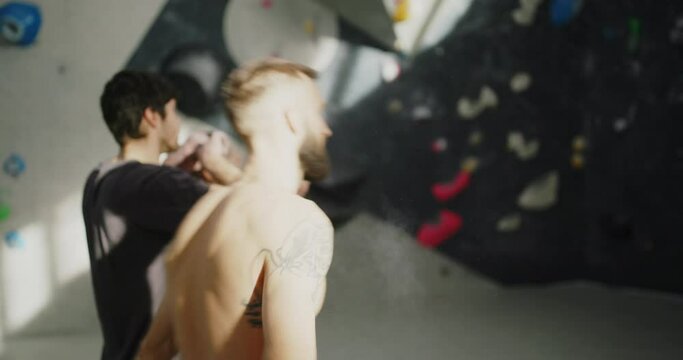 Muscular young man with tattoos jumping onto an artificial wall during climbing session with friends in a bouldering gym