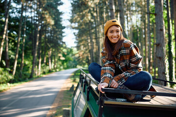 Happy woman on roof of camper van in nature looking at camera.