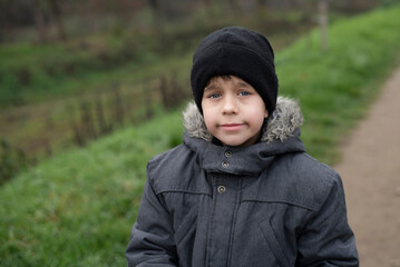 A young boy is warmly dressed during a walk in spring, he is already hot after active games in the fresh air, the boy is a little disappointed, he was waiting for dad and dad was late at work