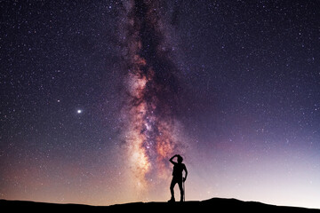 Silhouette of a hiker standing on the hill, on the milky way galaxy background. Cosmos wallpaper. 