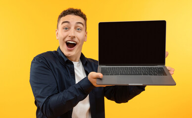 Happy young guy showing laptop with blank screen