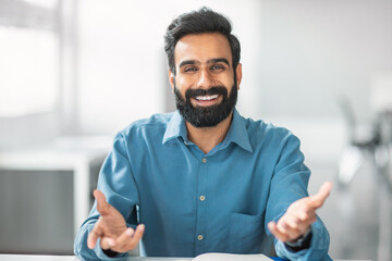 Cheerful indian bearded man in blue shirt smiling and gesturing at camera
