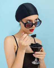 Young fashion woman eat black caviar from hand on blue background