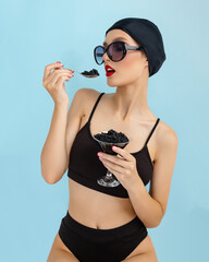 Young fashion woman eat black caviar from hand on blue background