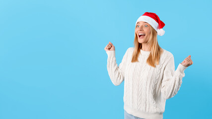 Fototapeta na wymiar Excited woman in Santa hat celebrating clenching fists