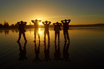 Silhouettes of people posing against the morning sky create a captivating beachscape.