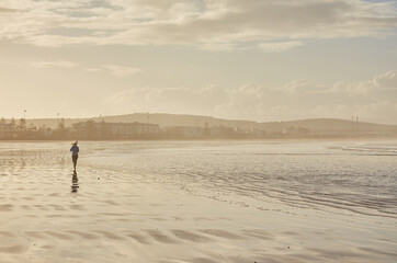 Fototapeta na wymiar A young woman embraces the tranquility of a seaside run along Essaouira's ocean