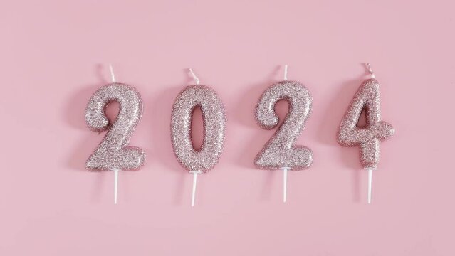 One set of new holiday glitter candles number 2024 lie in a row on a pink background, lay flat close up with zoom in.