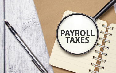 PAYROLL TAXES words on magnifying glass with pen and papers