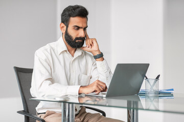 Serious indian businessman working on laptop at office